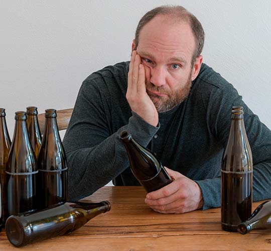 мужчина сидит за столом с большим количеством пустых бутылок